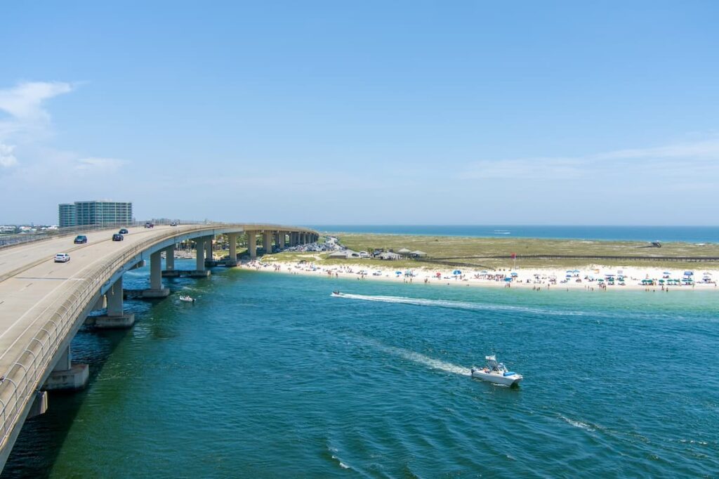 Boats passing underneath Perdido Pass and crowds gathered on beach in the distance